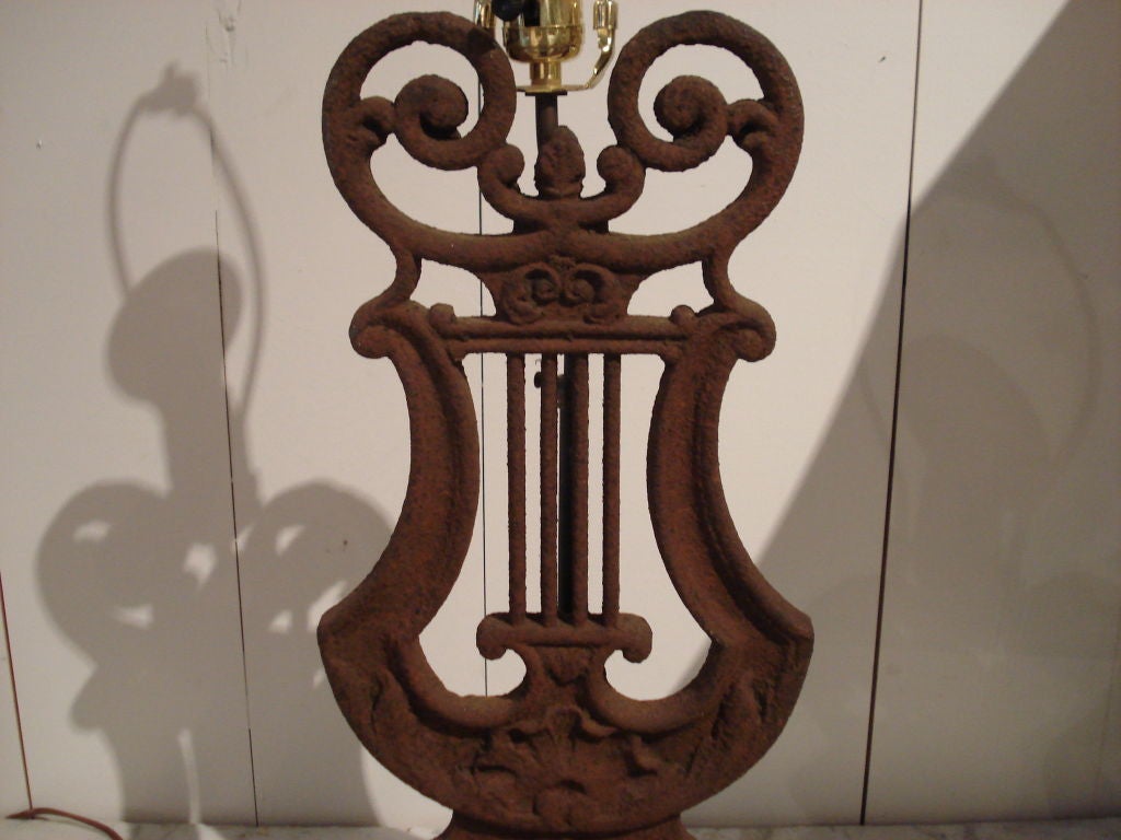 Pair of lamps made from Victorian fence pieces of Lyre-form. Set on stepped wood bases with finish to match the naturally rusted cast iron. Leaf form metal finials with  matching surface. Newly electrified for 3-way bulbs, with silk cord. Sold with