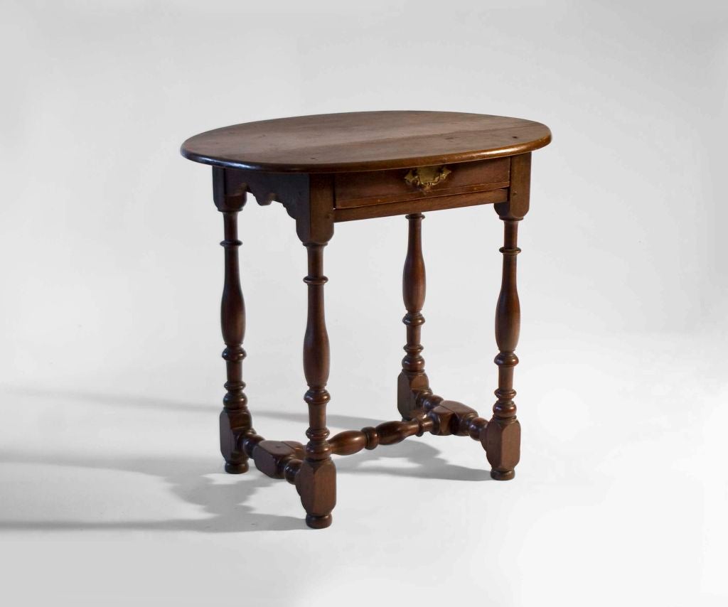 A truly exceptional tavern table of diminutive and highly turned proportions. This table is representative of early Queen Anne sophistication. An unusual oval top rests over a one drawer base with scalloped apron, four nicely turned legs with turned