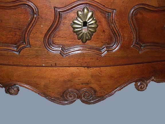 This shapely walnut commode of serpentine outline  has many indications of quality:  It has raised panels on the sides, it has a shapely apron, and well-carved scrolling feet. Despite its robust construction, its design with  many curved surfaces