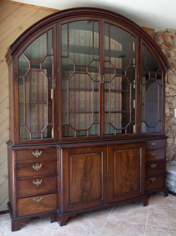 A substantial Cuban mahogany bookcase/cabinet in two sections: the lower of architectural, rectangular form with two projecting central doors (opening to reveal shelves) flanked by four graduated drawers (lined for silver); the upper section