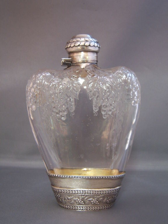 A rare and unusual sterling and crystal flask made by Tiffany & Co. Heavy crystal glass decorated with flowing grape vines, the flask topped with a vermeil interior sterling cap and standing in a detachable vermeil interior sterling cup .925-1000.
