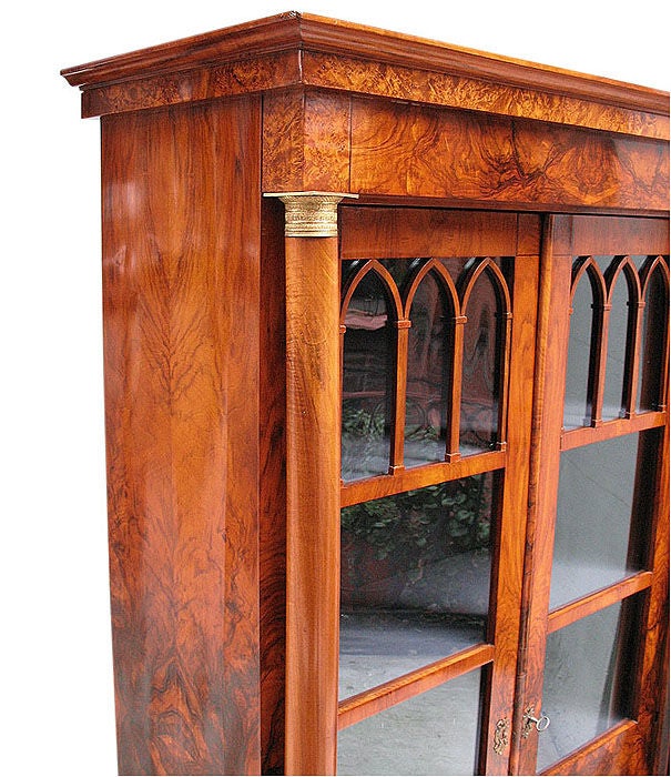 Exemplary South German Biedermeier vitrine. Two paneled doors with Gothic, pointed arch, grill work flanked by free-standing Corinthian columns supporting the cornice. Walnut on pine in book match pattern. All original condition including glasses,