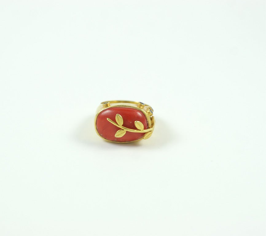 An 18kt yellow gold and coral ring. The ring is decorated with an 18kt yellow gold vine and bezel set sapphire buds.