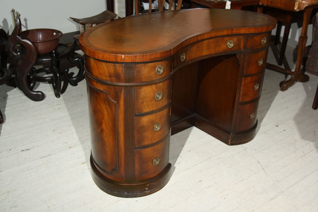 A KIDNEY SHAPED, LEATHER TOPPED DESK, WITH 9 DRAWERS AND OPEN  BOOK SHELF ON BACK