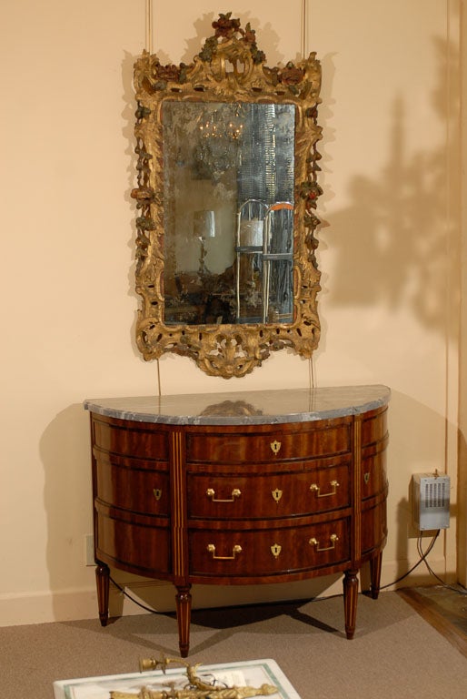 A late 18th century neoclassical mahogany demi-lune commode with  marble top.

The shaped grey veined marble top rests above a demi-lune form inlaid mahogany commode with three sliding drawers flanked on either side by doors and fixed with brass