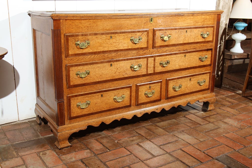 George III, pale oak, Lancashire mule chest with mahogany crossbanding on top and drawer fronts. Corners have reeded mahogany columns leading the eye down to ogee bracket feet flanking a scalloped apron. In typical mule chest fashion, the two top