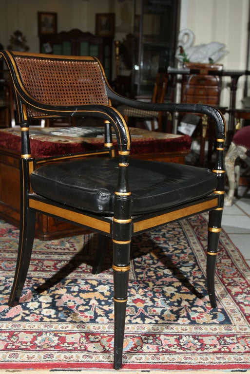 Pair of armchairs, ebonized with parcel gilt, faux bamboo form front legs, curved arms, and caned seats and backs. With tufted black leather cushions.