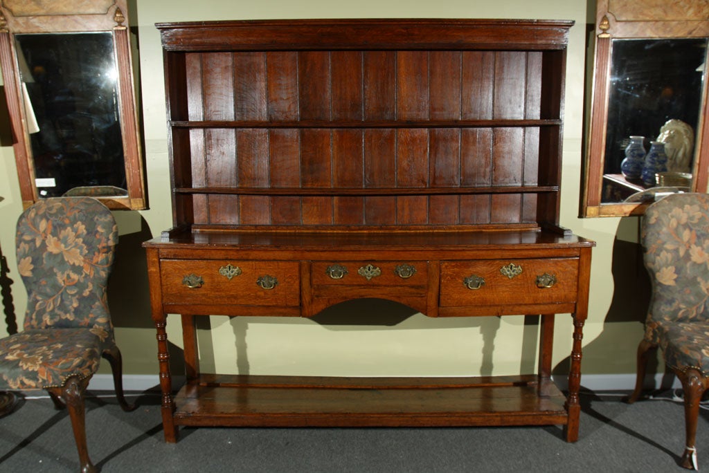 A hutch in oak with reeded frieze at the top, paneled back and three plate shelves over three apron drawers with brass hardware. A lower shelf with ring- turned supports and squared short legs.