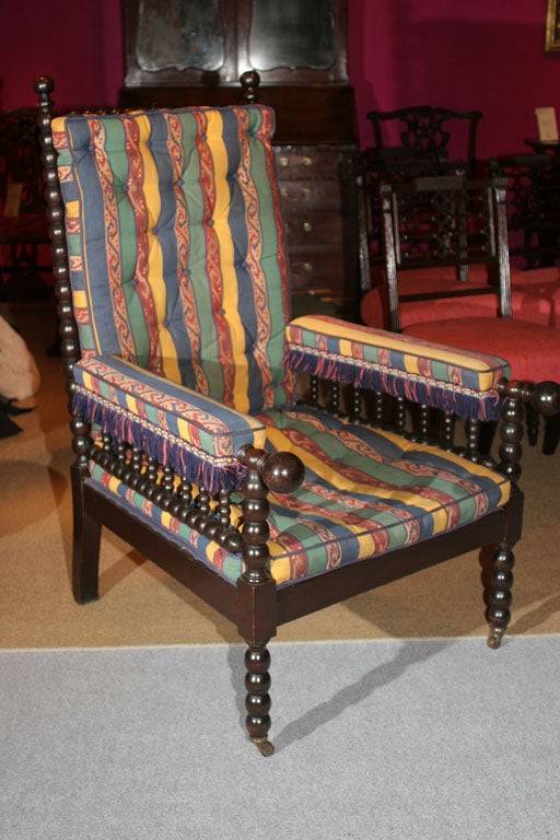 Very fine large-scale Renaissance Revival ebonized bobbin-turned armchair with finials to the top posts and as an unusual feature, posts extending from the arms, with polychrome tufted cushions and front wooden castors, English, circa 1870.