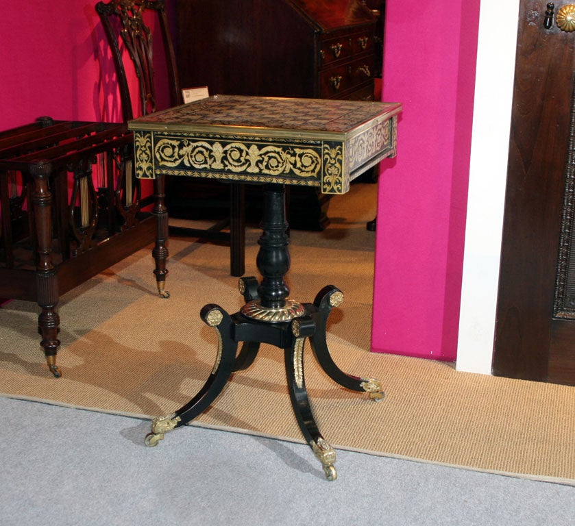 Very fine Regency period penwork games table, the chased brass bound square top with a board for chess or checkers above a single mahogany lined frieze drawer and two sliding trays to the sides to hold game pieces, the  ebonized base with a ring