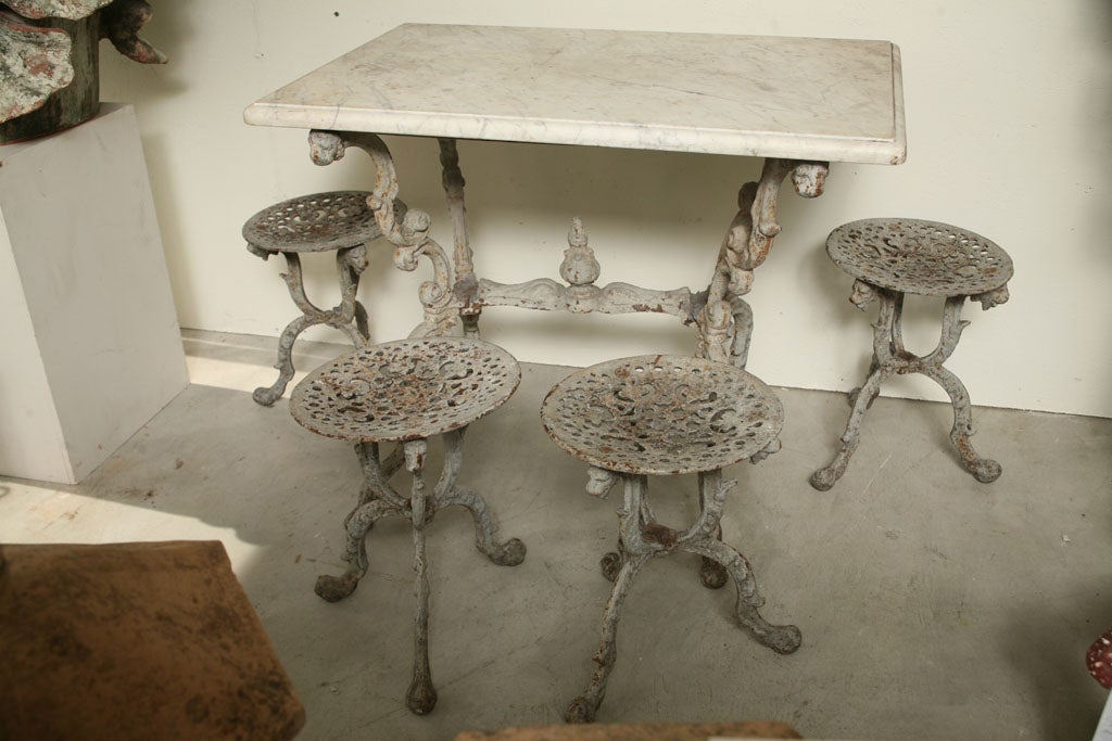 A suite of grey painted cast iron garden table with original white marble top, and four tabouret stools. Measures: Table W 35.5