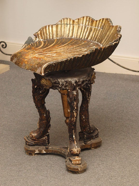 Three legged stool with the seat (which swivels) carved in the shape of a shell. The seat is supported on a round carved base adorned with gilt shells; the legs are carved in the shape of sea serpents and are mounted on a triangular carved wooden