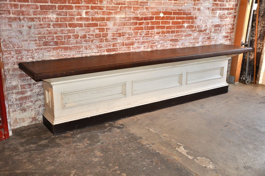 Sturdy general store counter found in Pennsylvania. Impressive form with great architectural detailing. Canted sides and top.  Original white and black paint. Smooth top and edges with an open back. Brass tacks along rear edge for measuring textiles.