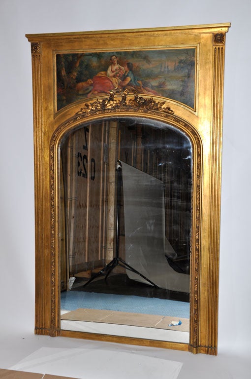 This lovely Louis XVI style gilded trumeau mirror has hand-carved onlay, as well as the classic oil painting above, featuring a couple in a garden scene. The large scale of this mirror makes it an eye-catching piece for a formal entryway or as a