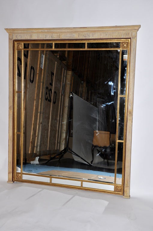 This large architectural mirror in the Neoclassical style features a molded cornice and pilaster sides. The large rectangular plate is surrounded by a gilt-wood border of inset panels which is cornered with rosettes. 
The large scale of this mirror
