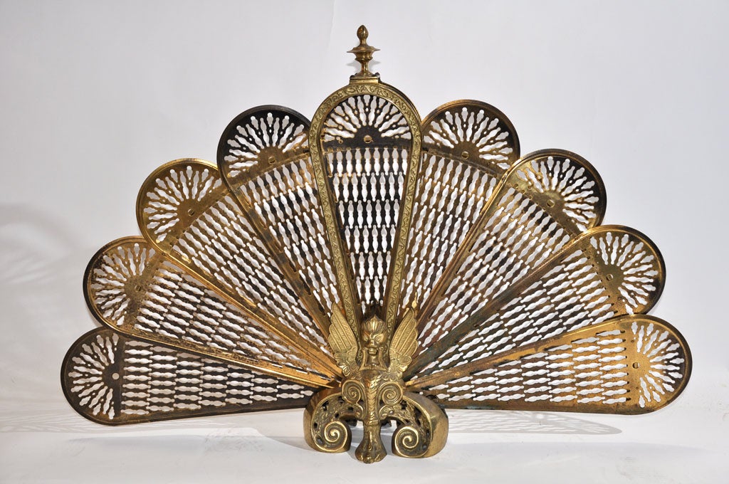 The brass fire screen opens in a fan pattern with scallop designs on each fan section.  The top has an acorn style finial.  Missing small hook on one side.