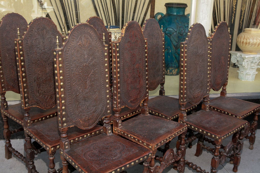Set of 8 high-backed dining chairs, Jacobean Revival style, in walnut, with stamped leather backs and seats, and brass studded and with brass finials.  Check out Tywin's Council Chamber for
the identical chairs in HBO's 'Game of Thrones'.
