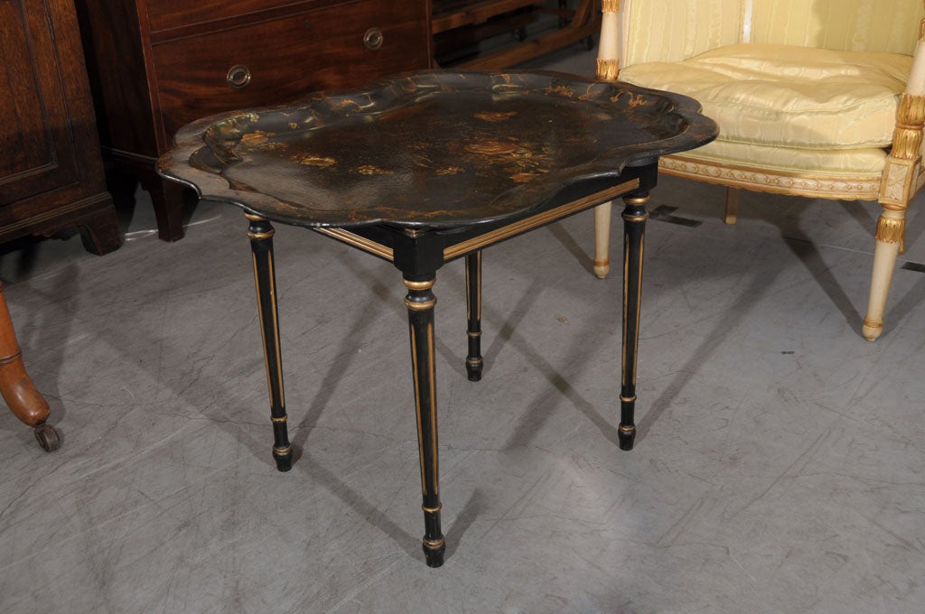 An English tray table or tray on stand, featuring a gadroon-edged japan-lacquered tray of papier mache with a recessed center showing a decorative oil painting of flowers, the edge with gilt accents. The tray fitted to a turned-leg stand in