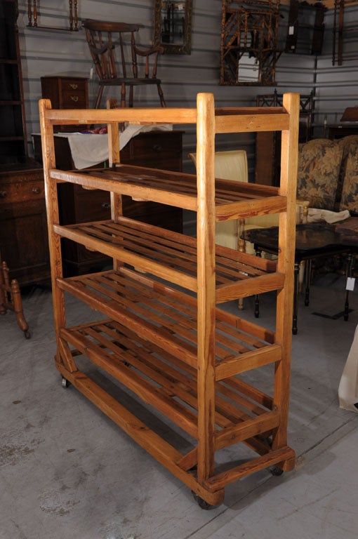 An industrial rolling trolley (rack) or display cart of long-leaf pine featuring five tiers of slatted shelves adjoined to a simple stretcher, resting on steel casters.