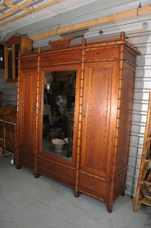 A handsome Faux Bamboo armoire of long leaf pine featuring a canopy of turned finials above a simple frieze of turned faux bamboo set upon three adjacent cupboards, each with a framed door, decorative brass escutcheon, and key. <br />
The center