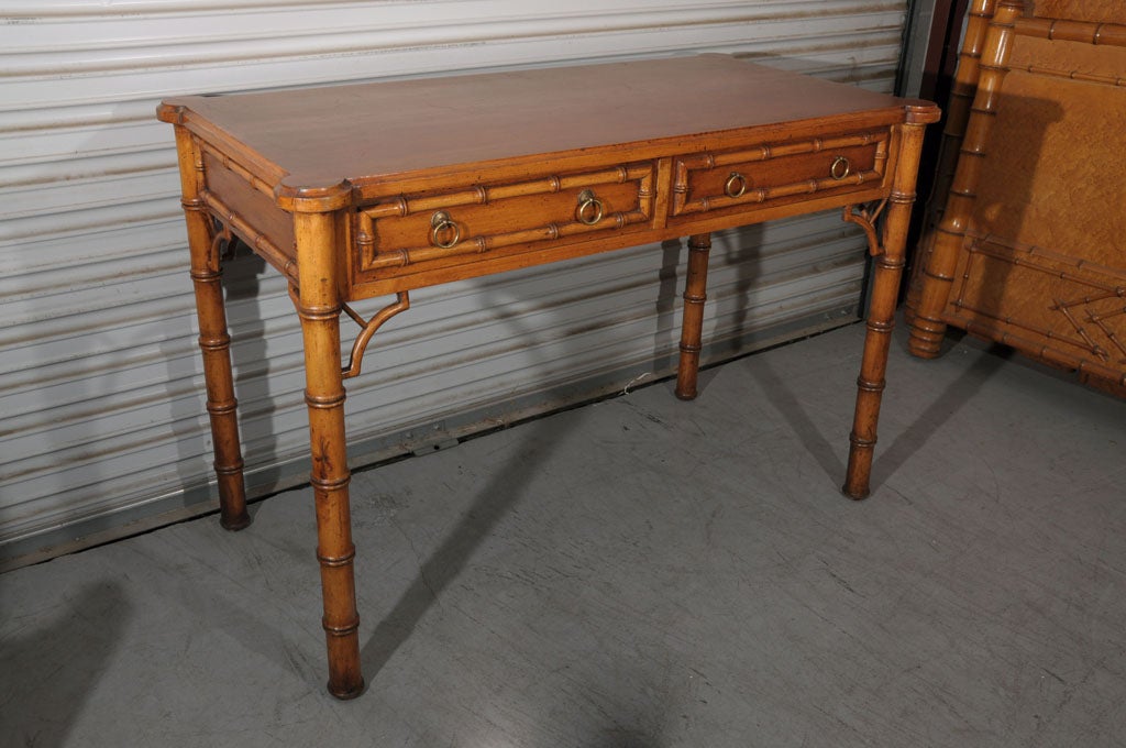 A handsome Faux Bamboo writing desk featuring a raised, moulded maple top over two short drawers, each with turned faux bamboo accents and brass ring pulls. Standing on four turned faux bamboo legs with Chippendale-style fretwork accents at each