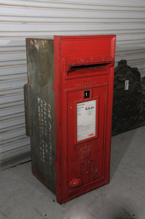 An English Royal Mail post box from Great Britain featuring a faceplate of red-painted cast iron attached to a mounting of cast iron.
The faceplate showing a mail slot with raised letters reading 