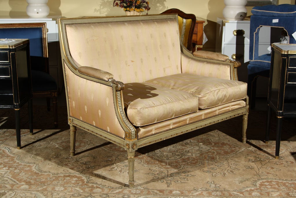 Painted and parcel gilded marquise with silk upholstery stamped Jansen. This Louis XVI settee or marquise is wonderfully detained and maintains its original distressed paint and parcel-gilt decorated finish. The ribbed arm rests indicative of this