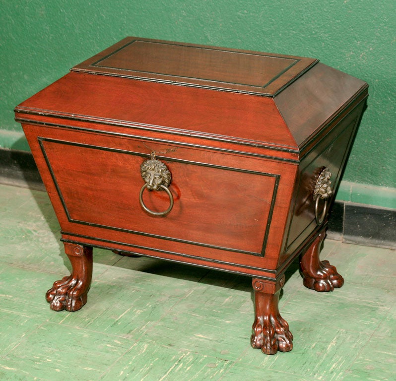 This mahogany cellarette with ebony inlay and molding shows great style. The sarcophagus form is raised up on boldly carved and dramatic Roman style lion paw feet giving the heavy case a lighter appearance while the flat planes of the sides and top