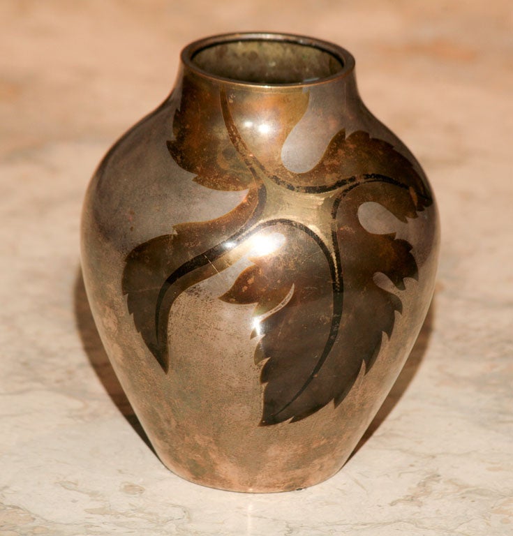 Here is a beautiful German Art Deco vase that is made of silver over brass. The leaf motif is elegantly rendered in tones of darkened brass and a bronze color. The vase has a nicely aged patina. The mark is barely legible but appears to be Ikora.