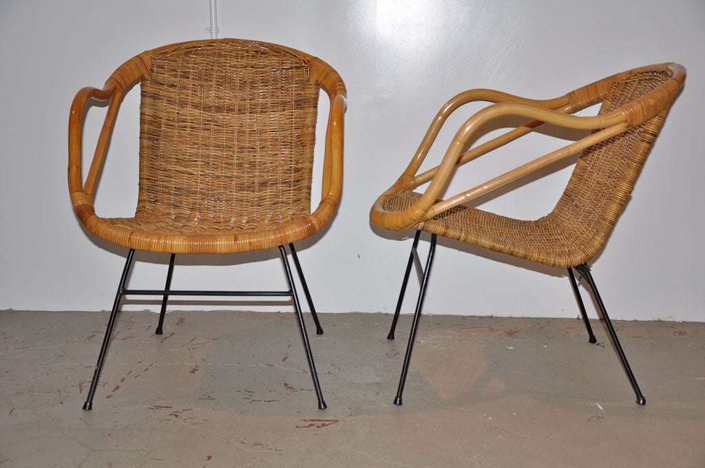Stylized pair of vintage rattan Hong Kong Ware side armchairs. Features a uniquely curved arm design and well-crafted tight rattan seat and back. Chair is supported by sturdy steel legs and frame. Price is for the pair.
