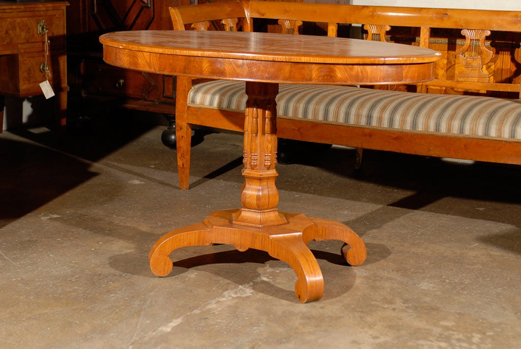 A gorgeous Swedish 19th century oval Karl Johan center table with carved pedestal resting on quadripod base. Elmwood and elm veneer. The Karl Johan period follows the Gustavian period in Sweden.