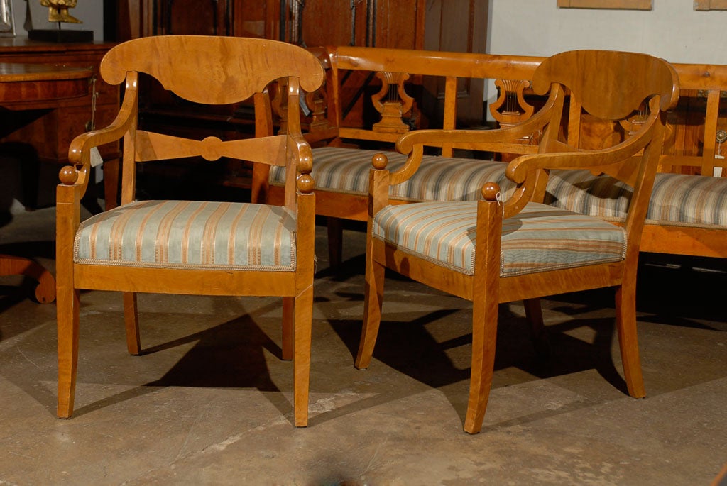 An exquisite pair of 19th century Swedish Karl Johan armchairs. This pair of Swedish Karl Johan birchwood armchairs from circa 1820-1830 features a nicely carved crest rail with curvy lines, scrolled arms joining the from legs topped with a ball