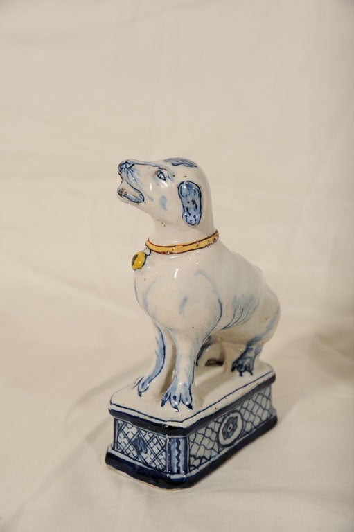 A pair of Blue and White Dutch Delft dogs have red and yellow collars with attached bells, and stand on typically stylized plinths.The dog is the emblem of faithfulness and guardianship.