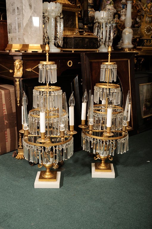 This pair of bronze girandole lamps have four electric candles and feature tall, cut-glass finals placed between each candle, and four concentric rings decorated with crystal and faceted jewel pendants.
Stock Number: L74.