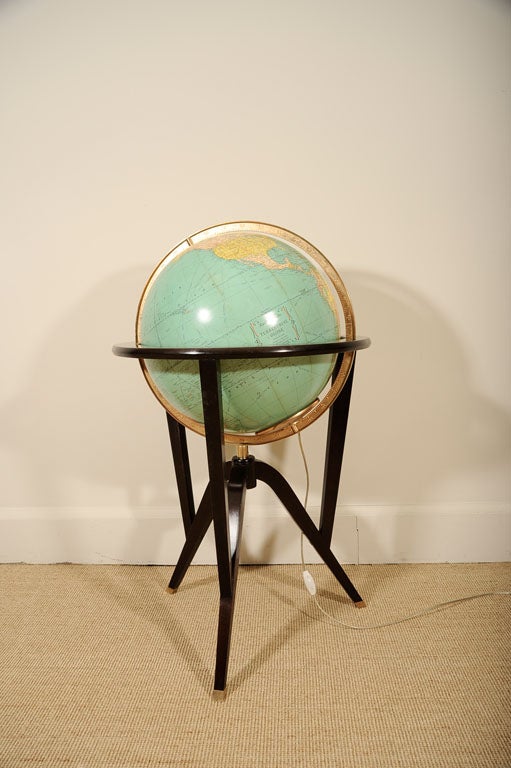 The globe with an internal light set in a brass ring with measurements, in a wooden frame raised on tripod legs with brass sabots.