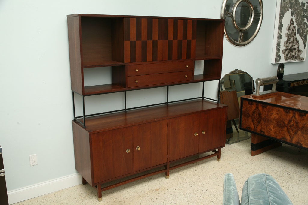 The superstructure mounted on an iron frame, the display cabinet sits on a credenza with open stretcher ending in brass capped legs. 
Inside storage drawers and shelf are features of the credenza.