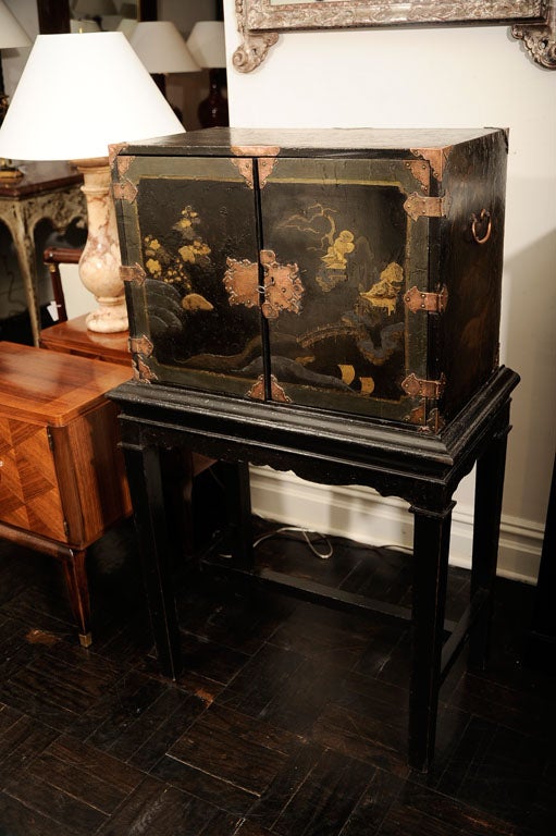 Mid-19th century chinoiserie black lacquer and gilt leaf design cabinet on later stand, gilt metal hinges and escutcheons on doors, interior has eight drawers, drop handles, square legs joined by cross stretcher.