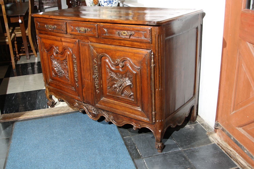French, carved cherry buffet with three-drawer over two-doors. Each door features high relief carving of an urn with flowers and this motif is repeated on the deeply scalloped and carved apron. Fluted and rounded corners lead down to elegantly