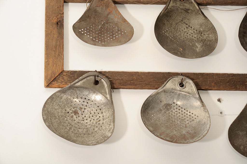 French cooking hand ladles arranged in 3 rows on wood lathing and iron hasps.