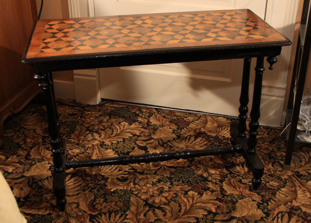 Table top with inlaid geometrical pattern of diverse timber having a three-dimensional effect. Top with carved finials underneath the apron is supported by turned ebonized legs, joined by a turned stretcher.

OFFERED AT THIS 50% OFF PRICE FOR 2015