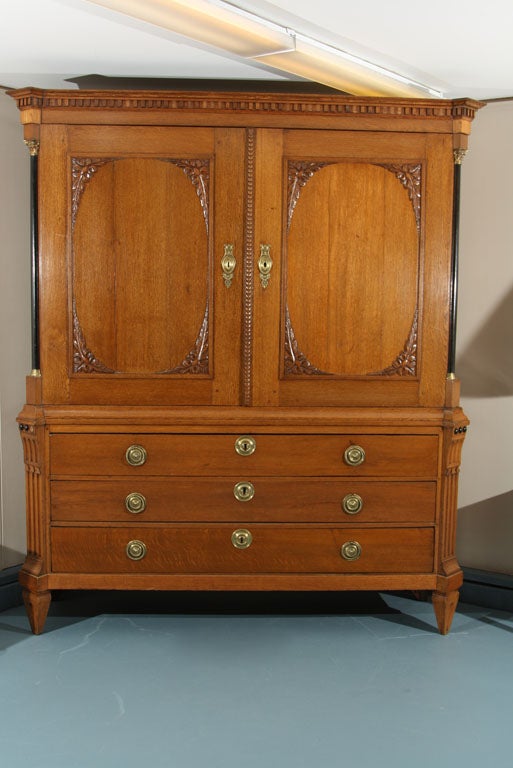 Large Dutch, pale oak linen press with applique mouldings on recessed panel doors, half column sides with ebonized treatment and having brass mounts over deeply fluted and chamfered base on spade feet. Interior features five shallow drawers while