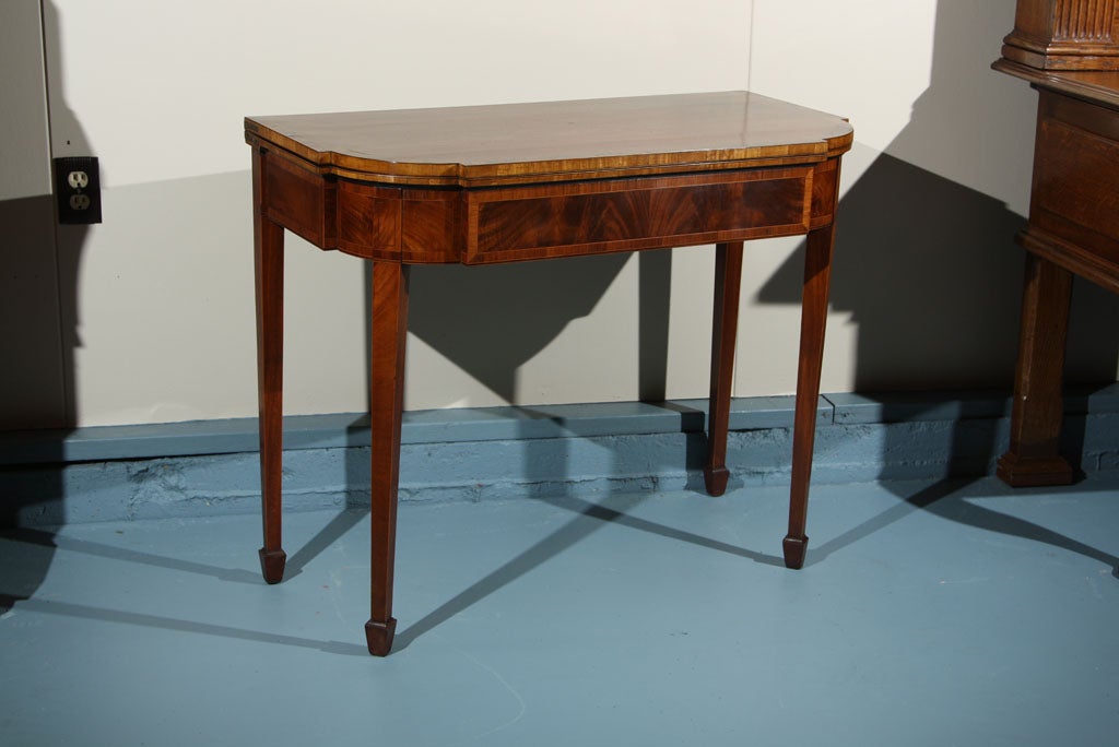 English mahogany flip-top Adam style game table on tapered legs ending in spade feet. Flame mahogany is used throughout with satinwood and rosewood bandings delineated by boxwood and ebony stringing. Felt playing surface is banded in rosewood.