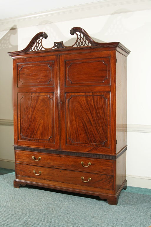 English, mahogany two-part George III linen press with fretted broken pediment over large doors having applied mouldings on well figured, solid mahogany panels; two large drawers in modified base, bracket feet.