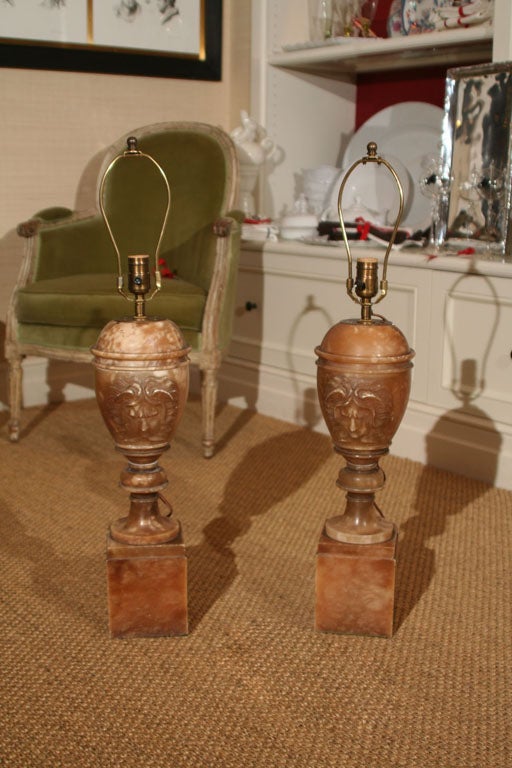 An exceptional pair of alabaster urn-form table lamps featuring central carved medusa on raised platform bases.