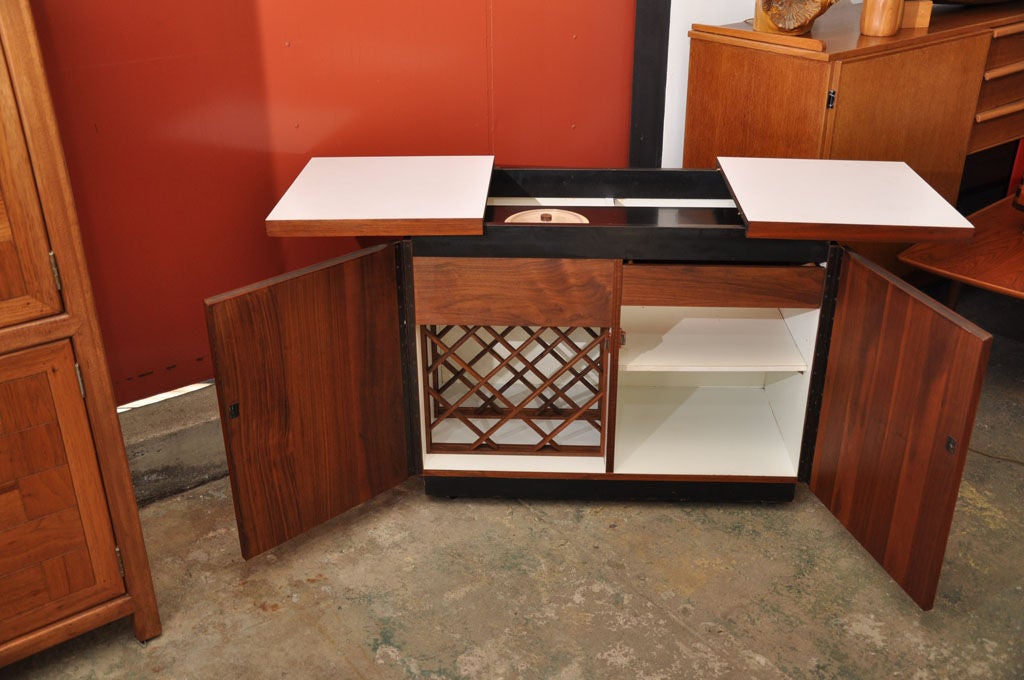 The white formica top opens on a container to store bottles and a removable ice bucket.<br />
In the bottom one door opens on a drawer and one shelf, the other one on a bottle rack.<br />
The base and the part underneath the top are black
