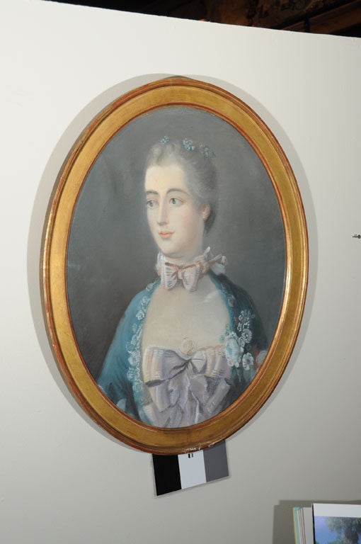 The fair completed woman depicted in this Classic oval portrait is very soft in nature. The gentle shades of lilac and gray are complemented by her richly hued turquoise jacket and gilded frame.