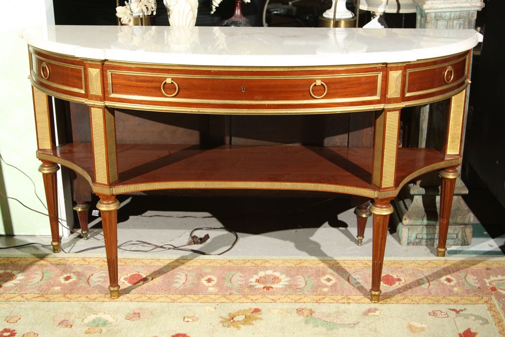 From our finest Jansen collection. Fresh from a private estate. A fine marble top mahogany console table, in the taste of French Directoire, the white triple-ogee half-moon marble over a frieze with a center long drawer flanked by two smaller
