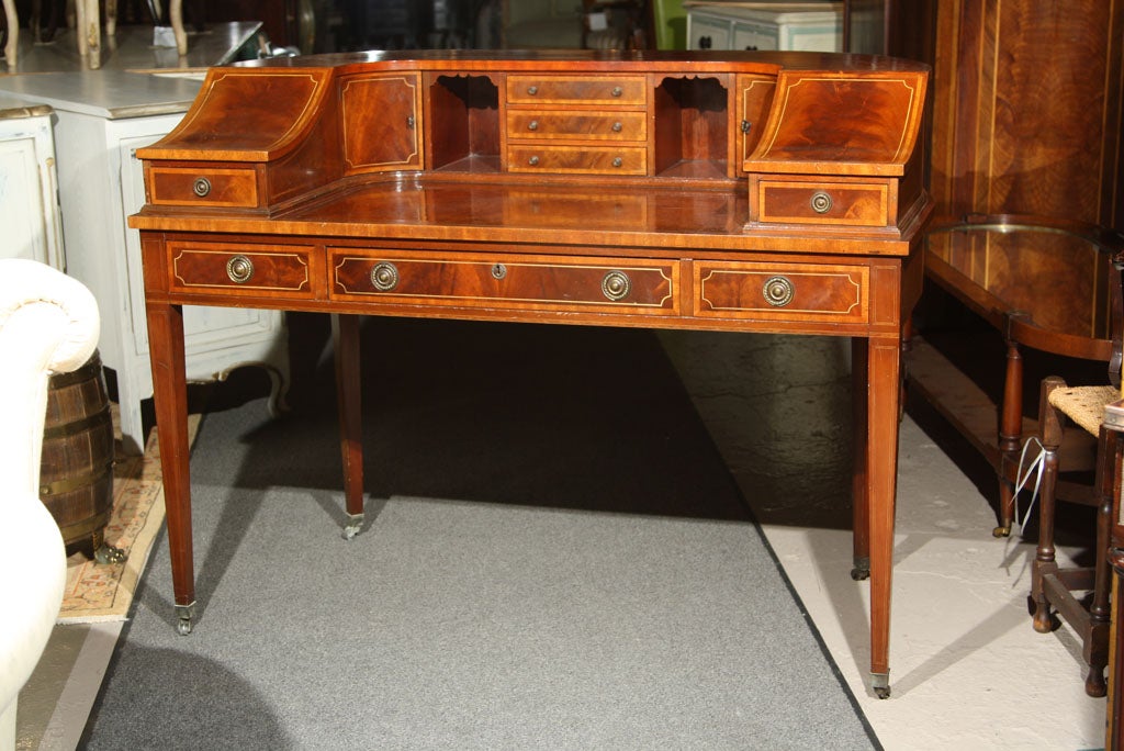 A fine custom quality banded crotch mahogany Carlton House Desk. The top compartments decorated with fine pencil inlays and banding sitting on tapering legs leading to brass casters.