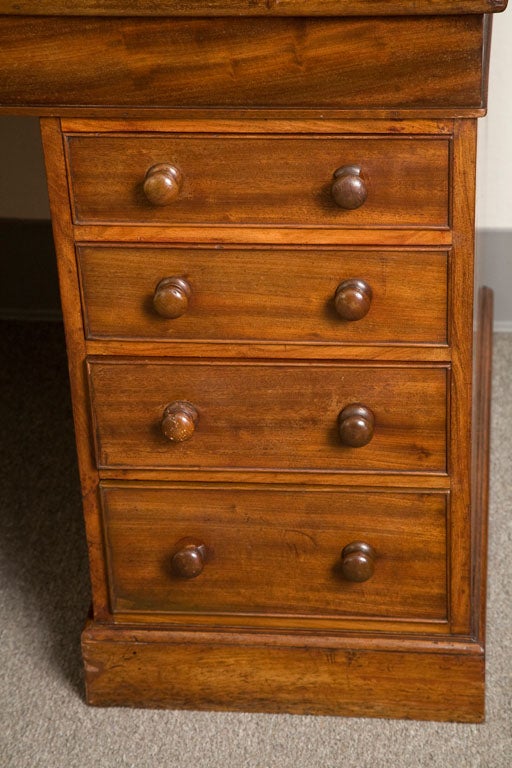 1850s English mahogany estate desk with molded cornice upper cupboard. The cupboard enclosing contains pigeon holes and shelves with a fall-front writing surface and eight drawers on a plinth base.