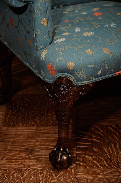 The arched back, outscrolled sides and bowed seat covered in blue fabric woven with flowering vines, raised on strapwork-carved cabriole legs ending in ball-and-claw feet, the back legs carved.
